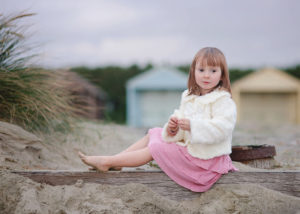 Girl on sandy beach infront of beach huts by Moira Lizzie Photography
