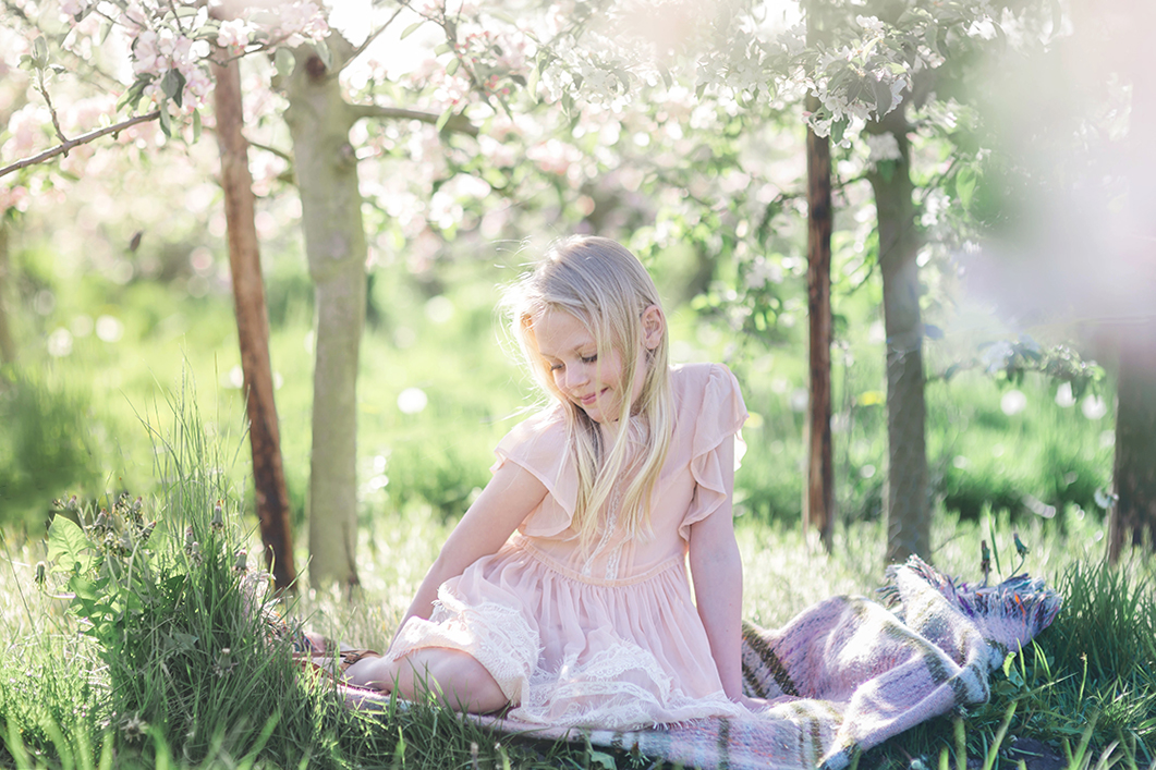 Spring portrait of girl sitting on picnic blanket in orchard blossom by Moira Lizzie Photography