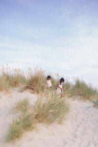 Sisters climbing sand dune at West Wittering Beach