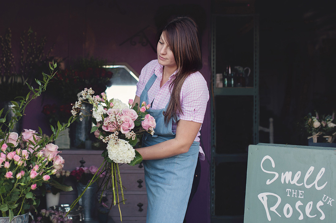 Personal branding image of florist in apron arranging a bouquet in her workshop doorway