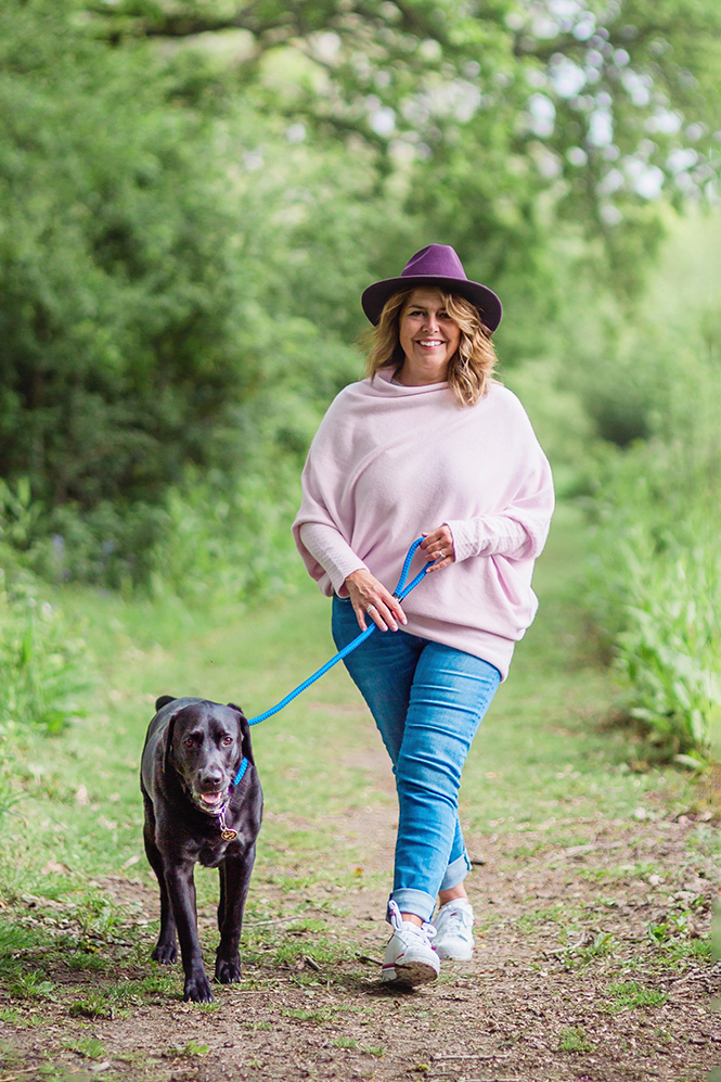 Personal branding image of business owner relaxing by walking her dog. She's wearing jeans, a pink jumper and purple hat